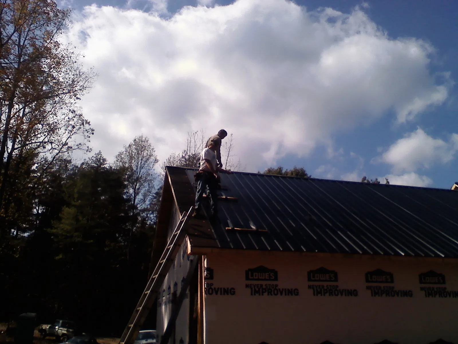 Roofer fastening dark metal panels high against a cloudy sky, from a Roof Inspection job in Monteagle