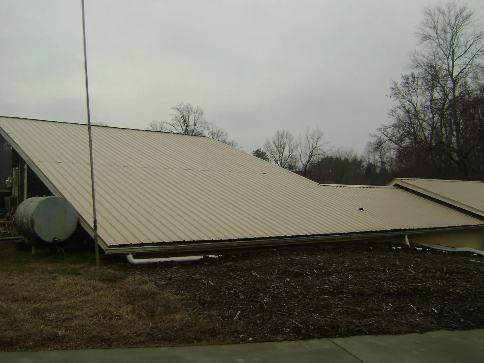 Wide tan metal roof plane seen from the ground beside a propane tank in Monteagle