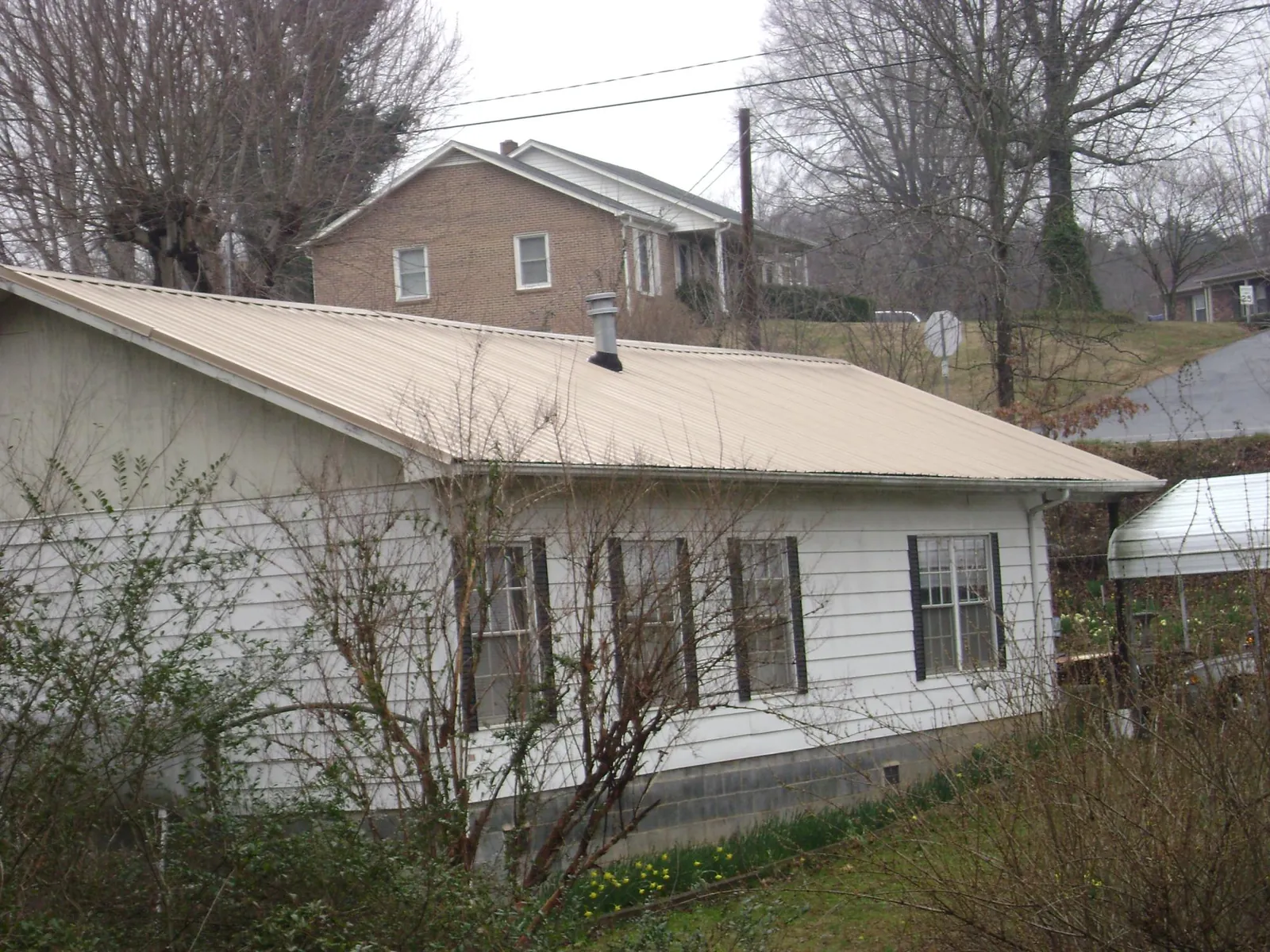 Tan metal roof on a white sided house set into a hillside — Commercial Roofing by Roofing Brothers in Monteagle